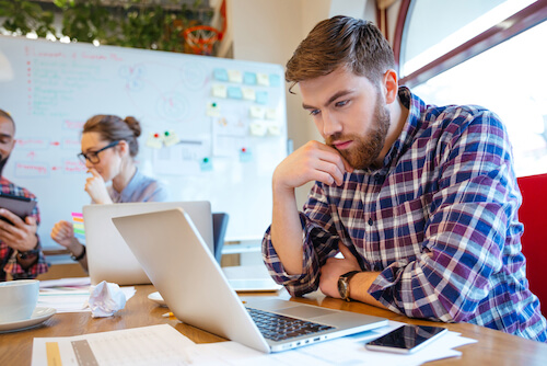 Concentrated bearded young man using laptop while his friends studying together