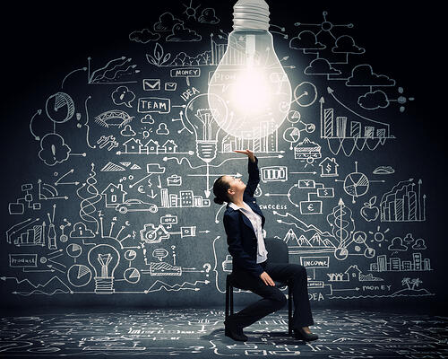 Young businesswoman sitting on chair with big light bulb above